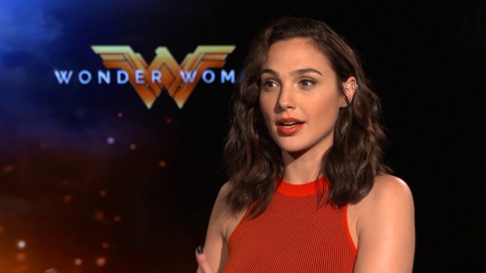 Gal Gadot sitting by Wonder Woman logo - MyConfinedSpace